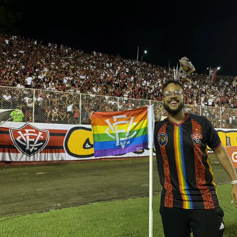 Integrante da ORN dentro do campo do Barradão, ao lado da bandeira arco-íris do Vitória no escanteio